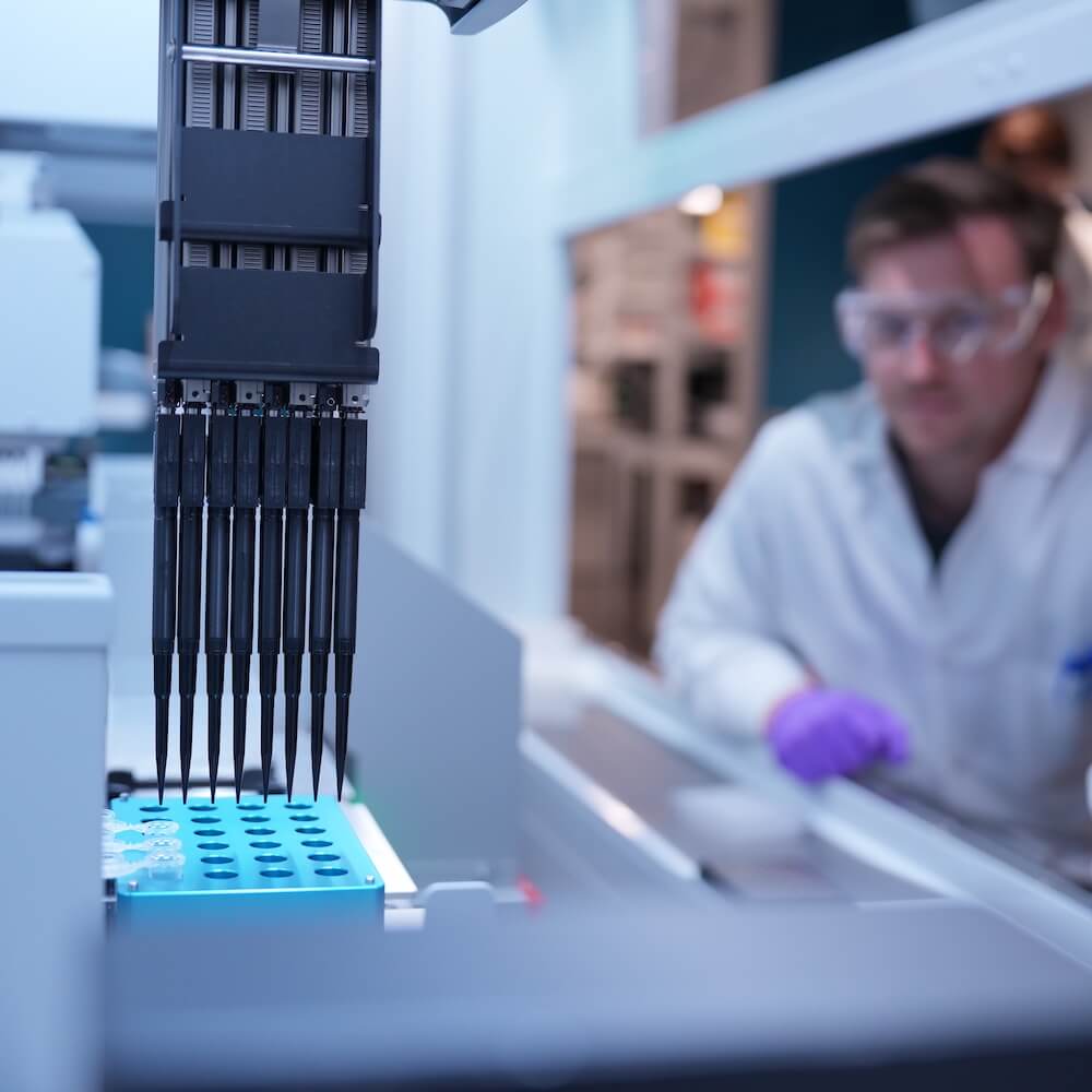 Beautiful editorial photo of researcher in background with liquid handler in foreground.